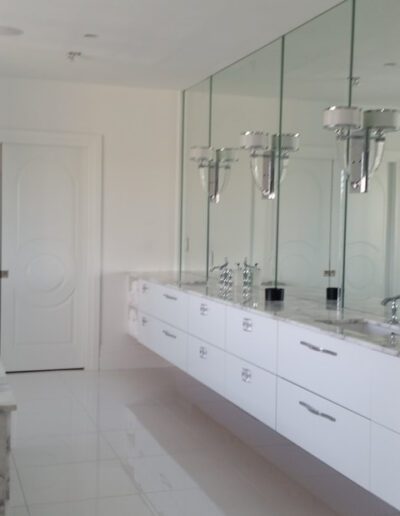 A modern bathroom with marble walls and floor, featuring a large mirror, double vanity, and a bathtub.