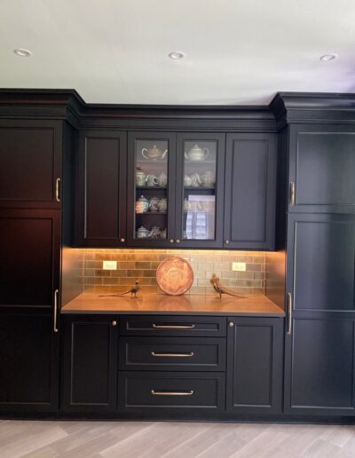 Elegant black kitchen cabinetry with under-cabinet lighting highlighting a tiled backsplash and glass-front display cabinet.