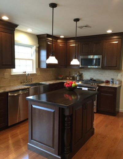 A modern kitchen with wooden cabinets, stainless steel appliances, hanging pendant lights, and a central island.