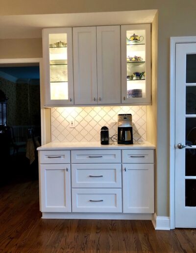 A well-lit kitchenette with white cabinetry, a coffee maker, and a tiled backsplash.