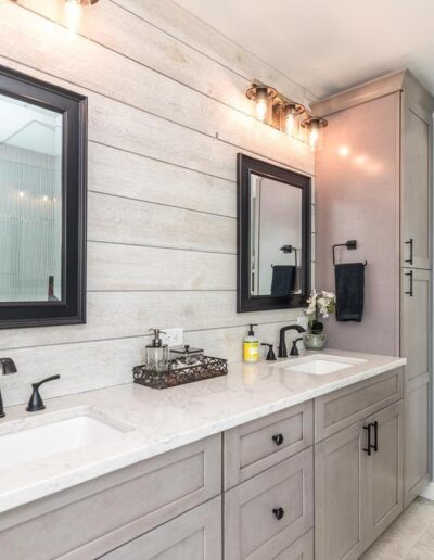 A modern bathroom interior with double sinks, large mirrors, and a view into an adjoining bedroom.