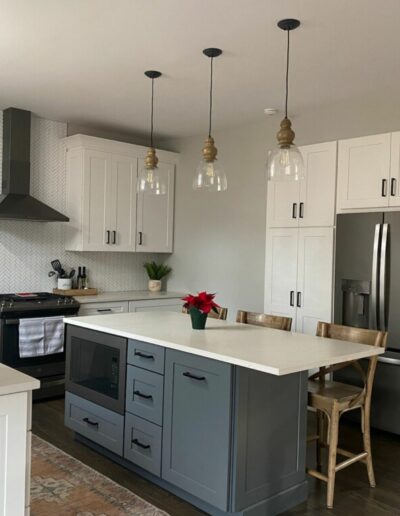 Modern kitchen interior with white cabinetry, stainless steel appliances, and a gray island with pendant lighting.