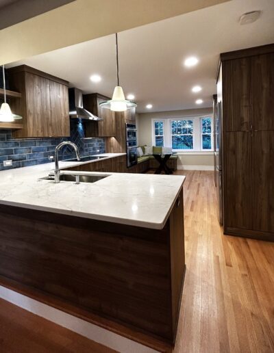 Modern kitchen interior featuring wooden cabinets, stainless steel sink, pendant lighting, and hardwood flooring.